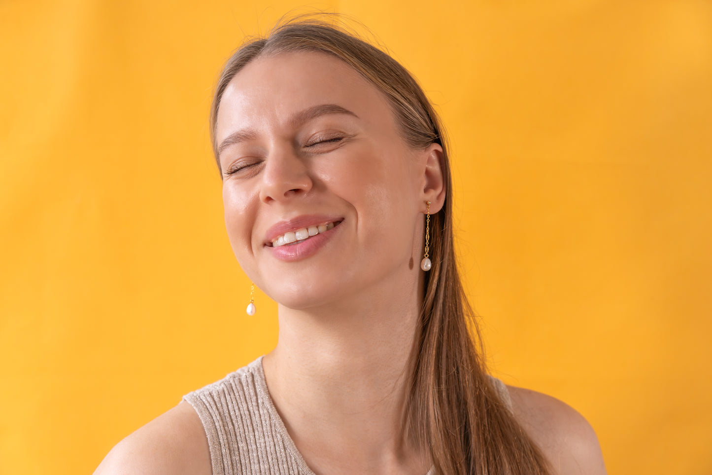 Woman wearing gold earrings with baroque pearl pendants against a yellow background