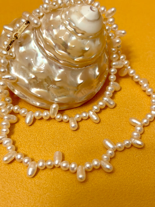 Aurora Luster Wild Keshi Pearl Choker Necklace displayed on a seashell with vibrant orange background.