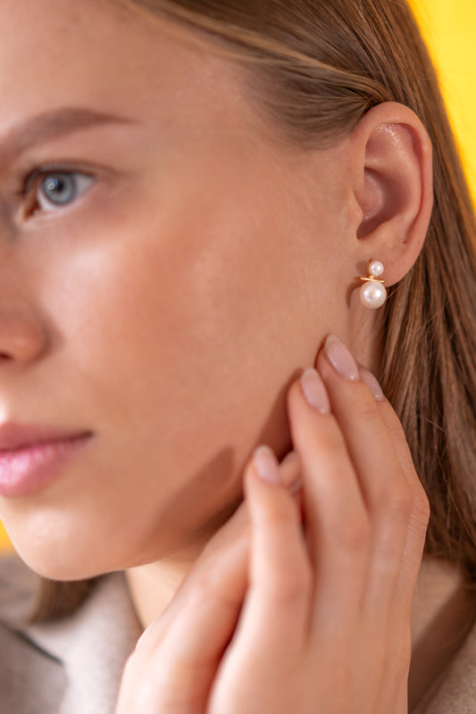 Close-up of a woman wearing white pearl earrings with a neutral background