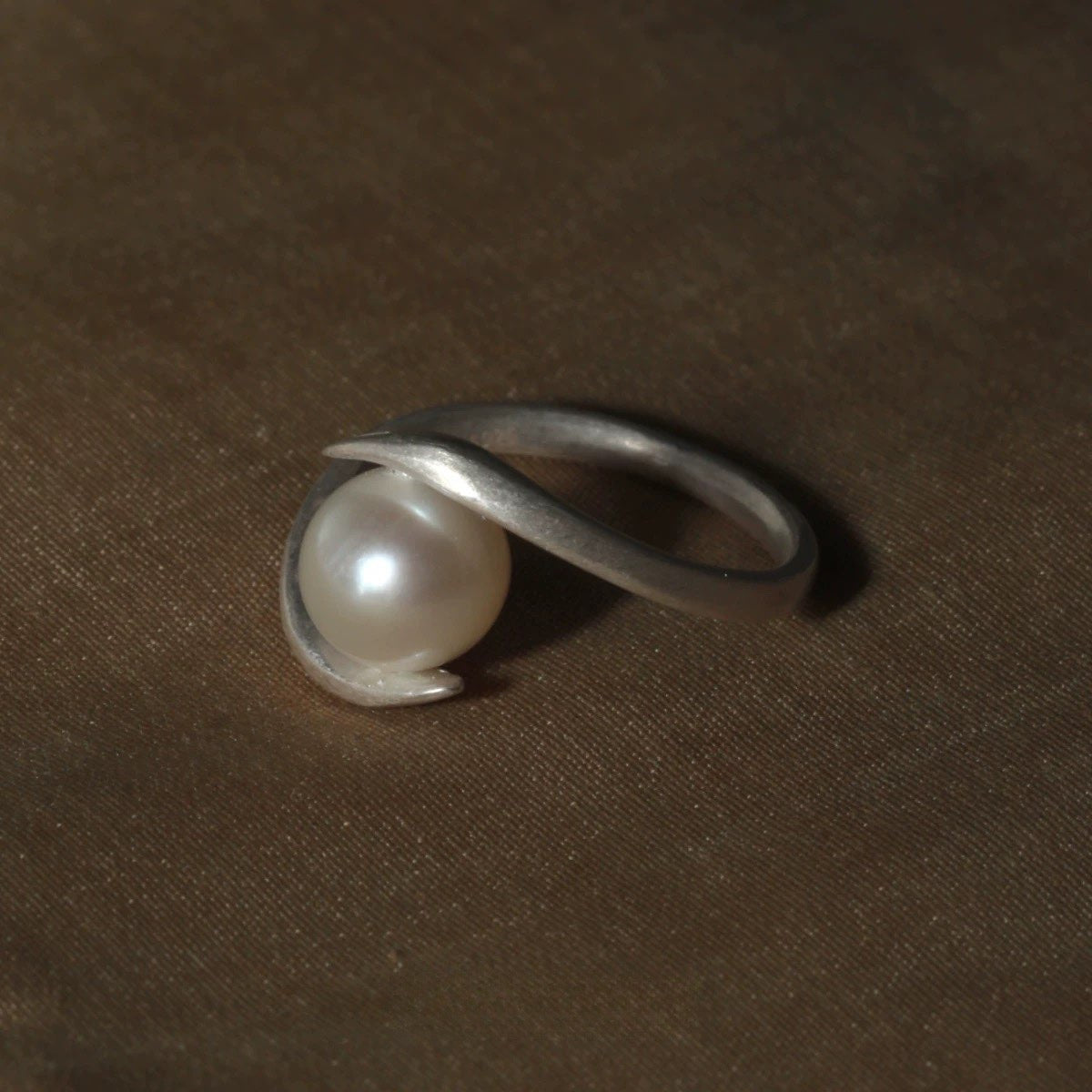 Silver ring with a pearl on a brown fabric background
