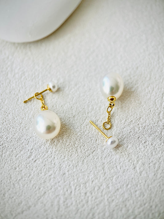 Pearl earrings with gold hooks on a textured white surface