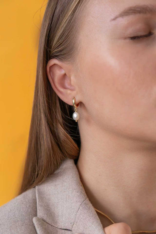 Close-up of a person wearing white baroque pearl earrings against a yellow background