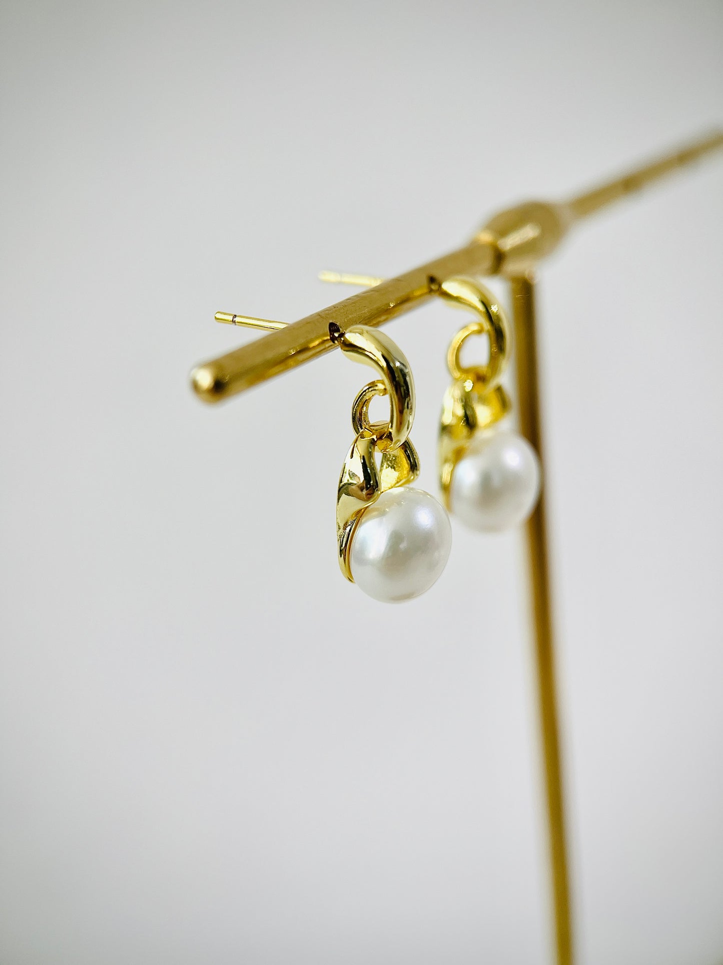 Gold earrings with pearl drops on a light gray background