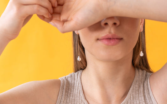 Woman wearing long gold pearl earring with a yellow background