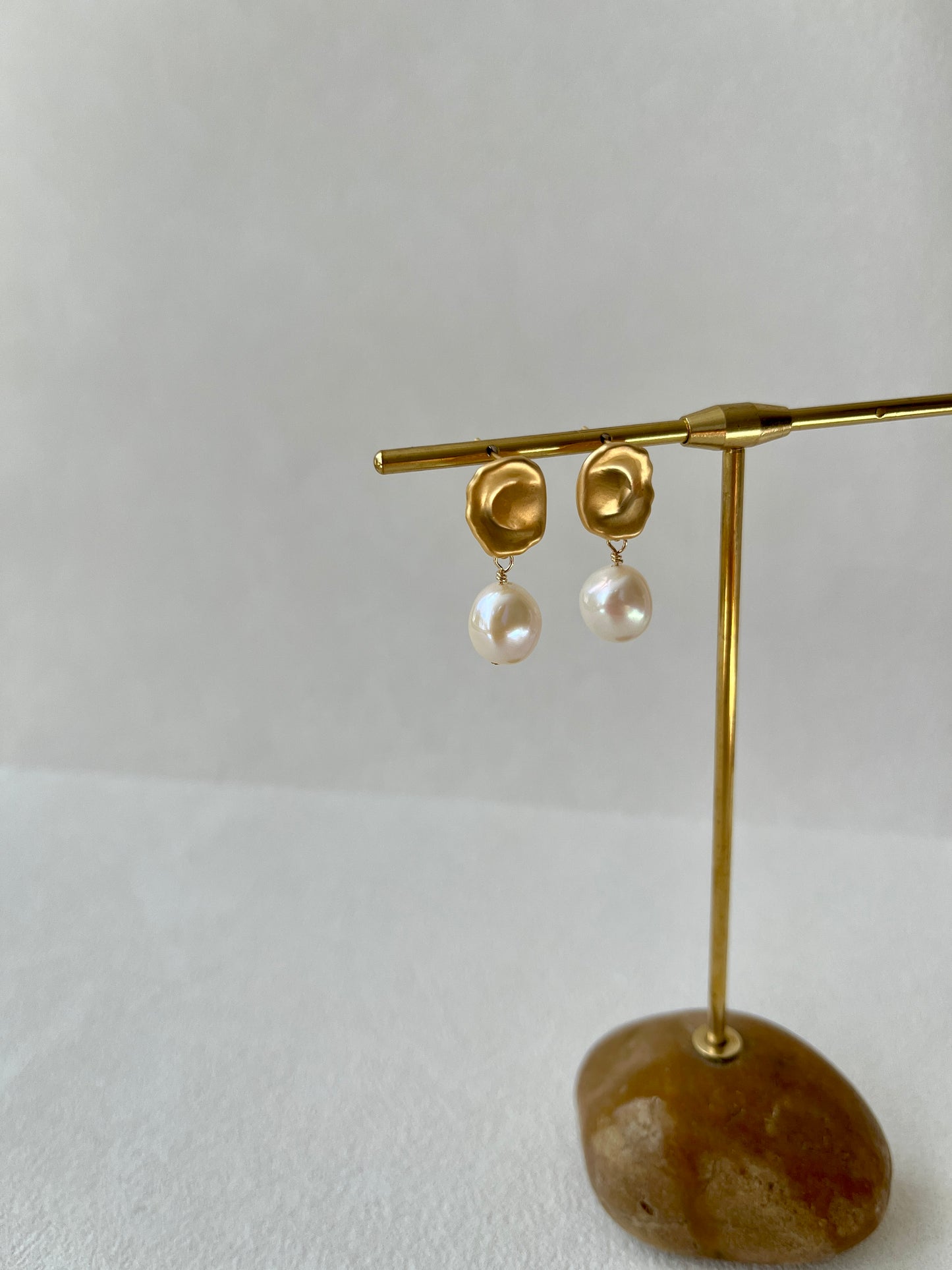 Gold earrings with pearls on a wooden stand against a white background