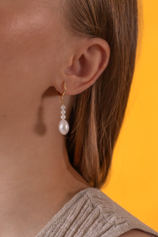 White Freshwater pearl earrings worn by a person with a yellow background