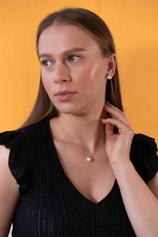 Woman wearing a black top and pearl necklace against an orange background