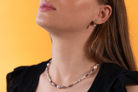 Close-up of a woman wearing a purple pearl necklace and keshi purple earrings against a yellow background
