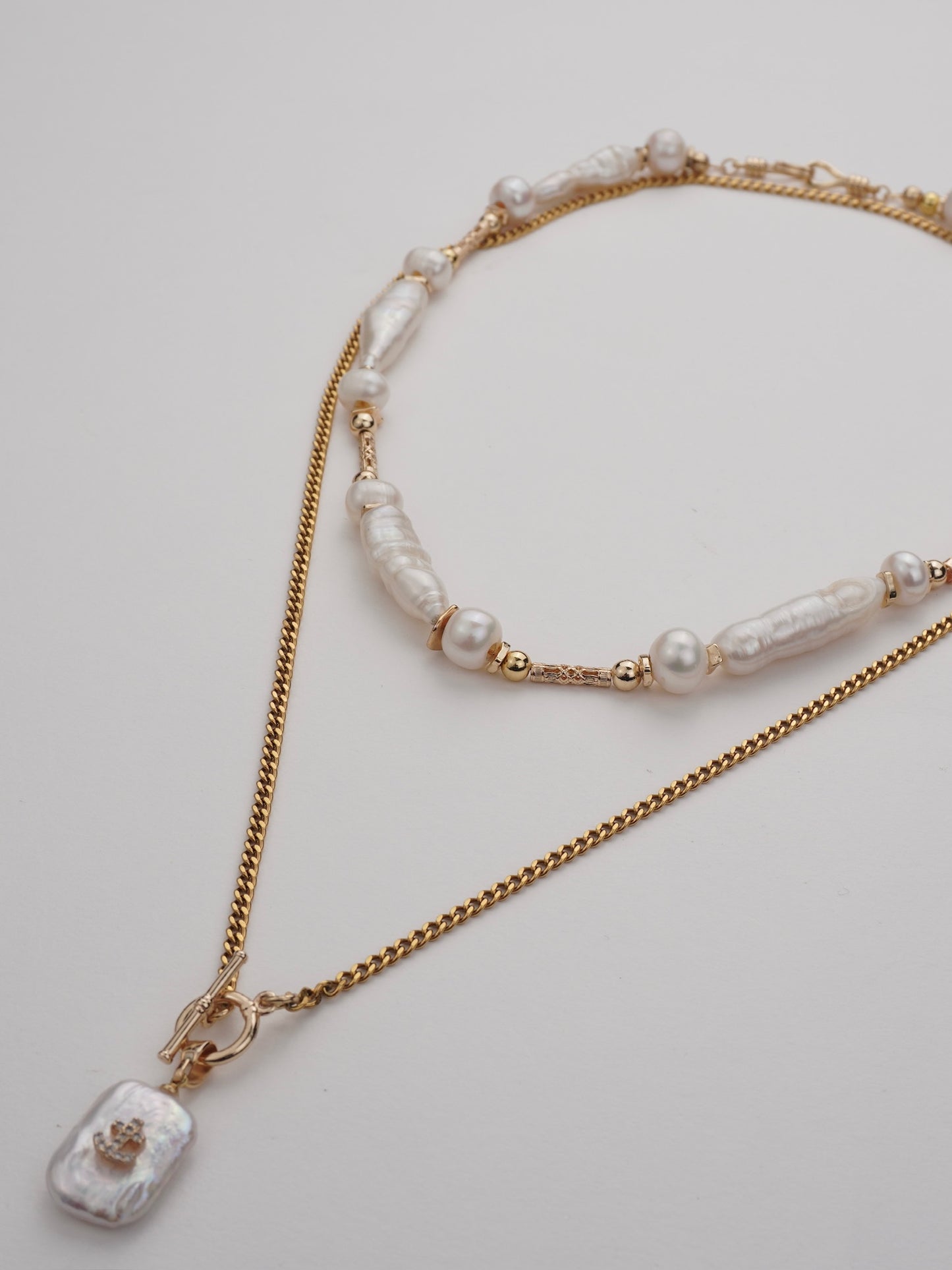 Two gold necklaces with pearl beads and a pendant on a light gray background