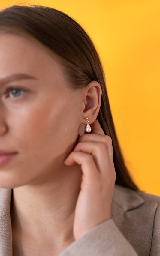 Woman wearing a gold pearl earring with a yellow background