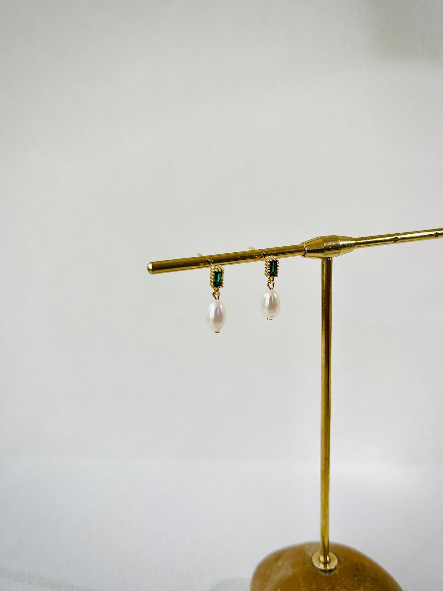 Gold earring stand with three earrings on a light gray background