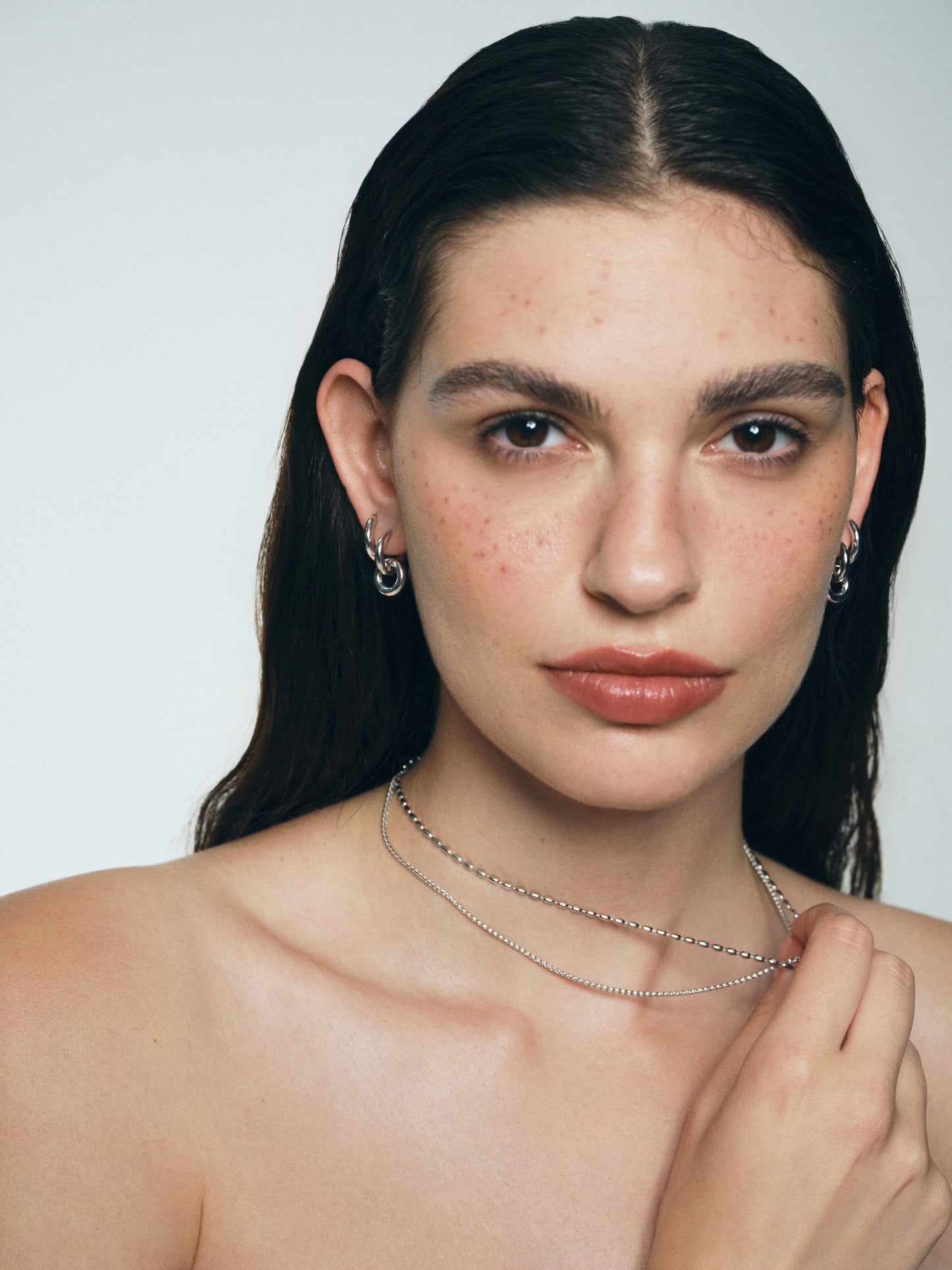 Woman with long dark hair wearing a necklace and Rhodium-plated silver earrings against a plain background