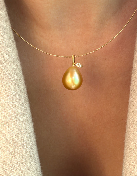 Gold necklace with a teardrop-shaped or pear shaped pearl pendant on a person wearing a beige sweater.