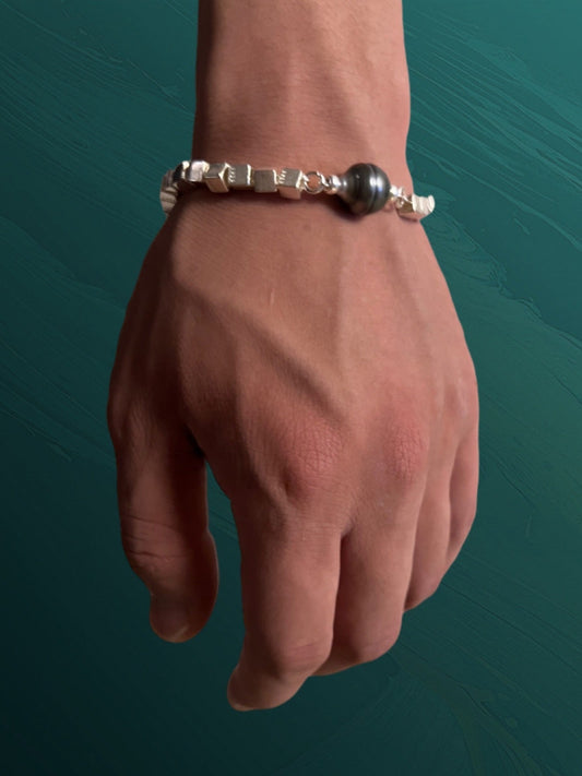 Hand wearing a tahitian pearl silver bracelet on a teal background