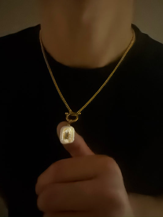 Gold necklace with a pearl pendant worn by a person against a dark background