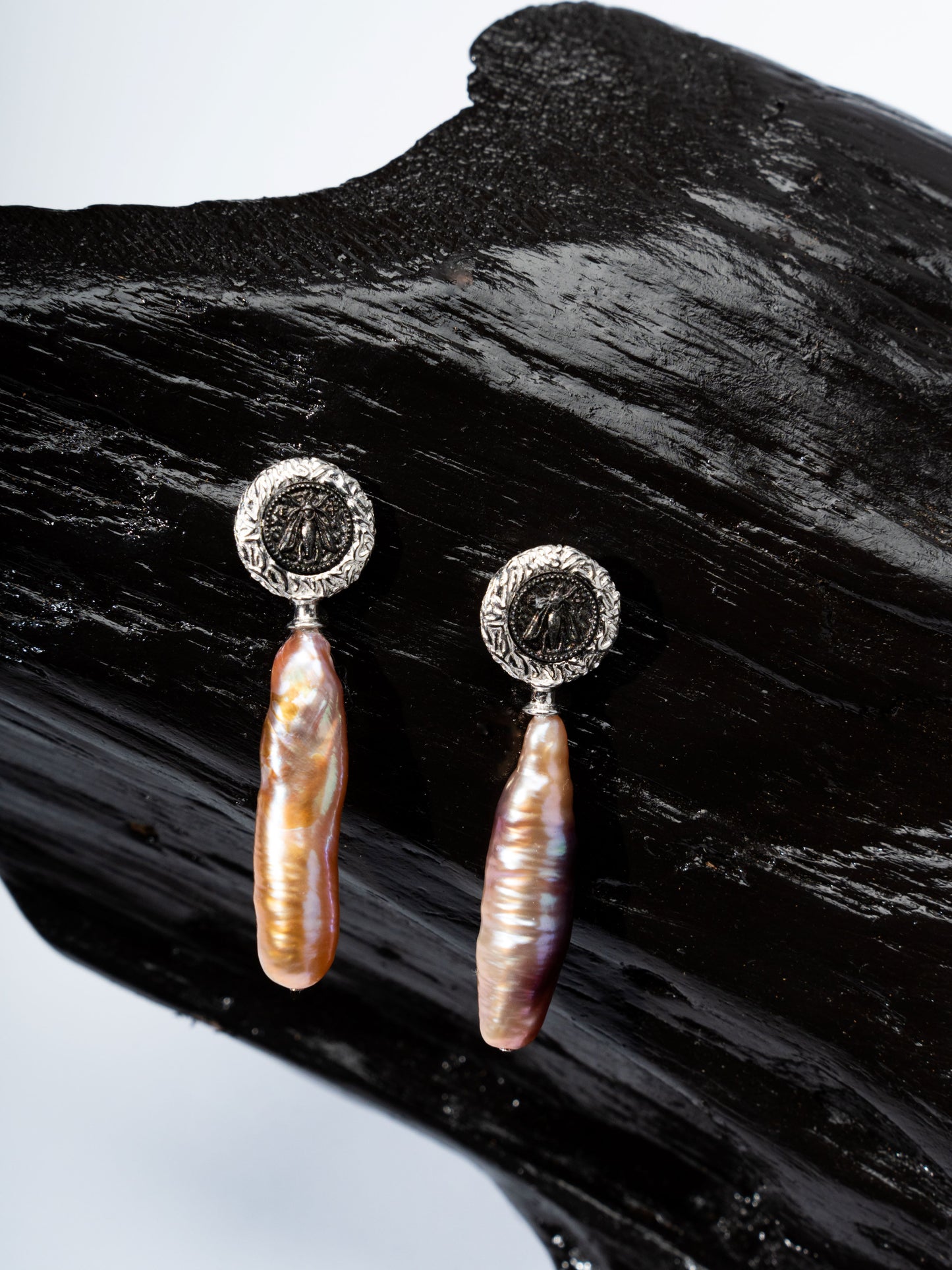 Pair of baroque pearl earrings with silver circular tops on a dark wooden surface