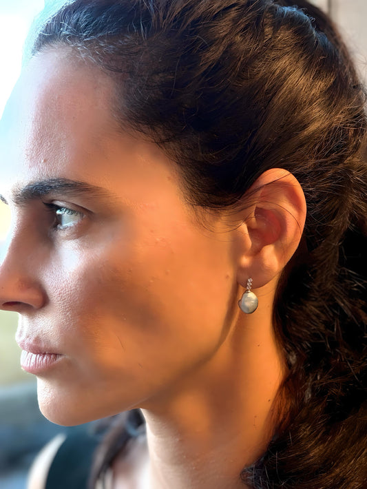 Close-up of a woman wearing Tahitian Keshi pearl earrings suspended in 18K white gold with a blurred background