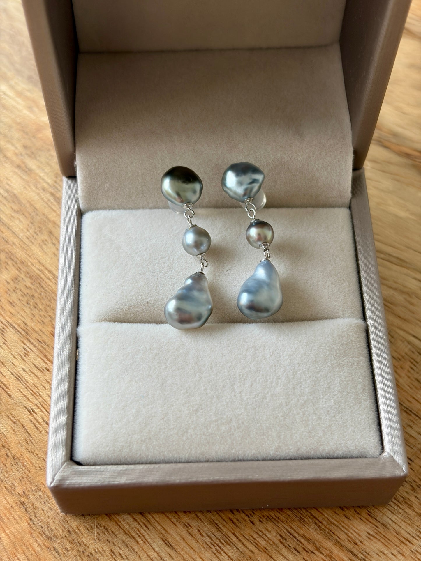 Pair of Tahitian Keshi pearl earrings in a jewelry box on a wooden surface