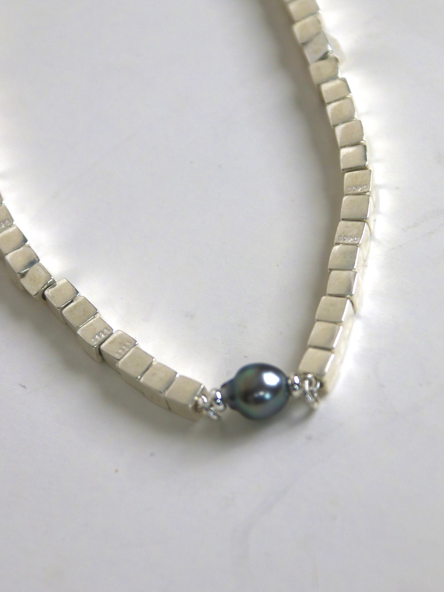 Bracelet for men with white beads and a dark Tahitian pearl on a light background
