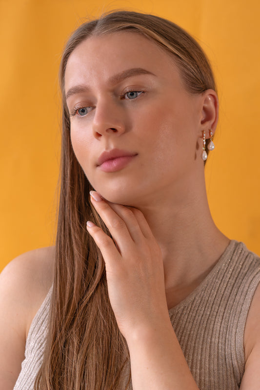 Woman wearing gold baroque pearl earrings against a yellow background