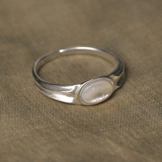 Silver ring with a central nacre stone on a beige fabric background