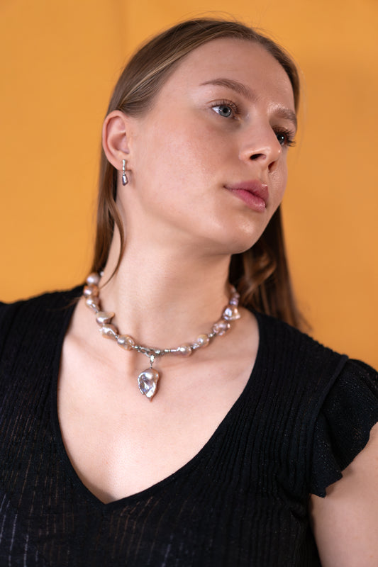 Woman wearing a purple pearl necklace with a pearl pendant against an orange background