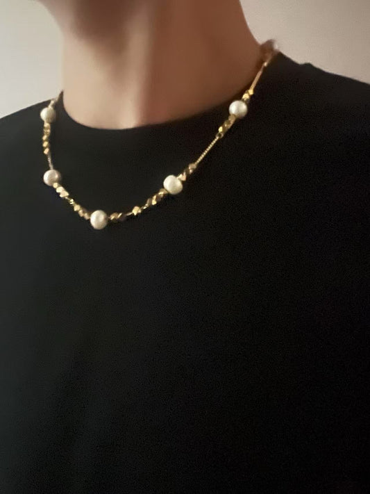 Pearl necklace on a person wearing a black shirt against a neutral background