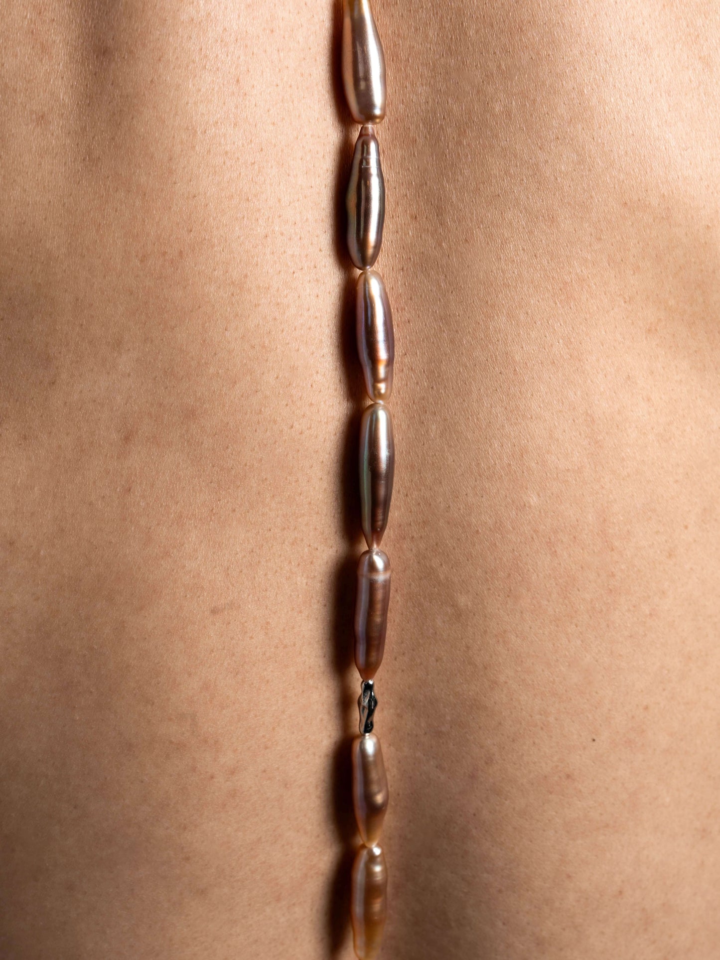 Close-up of a necklace with pearls on a person's neck against a neutral background