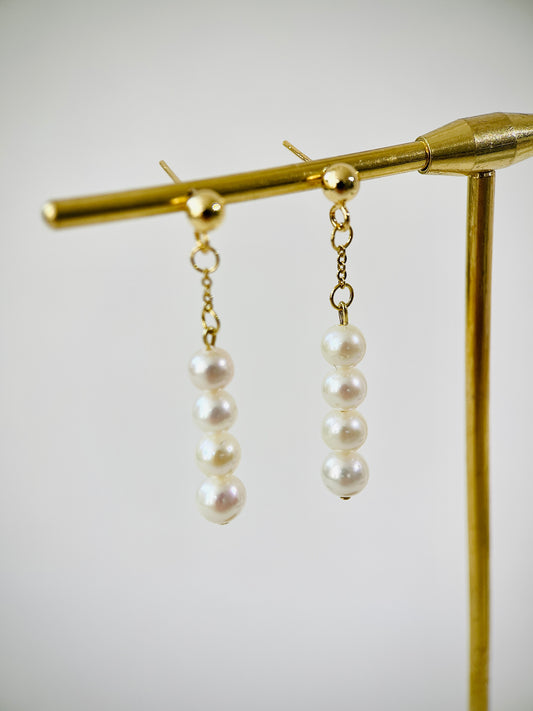 Pearl earrings on a gold stand against a white background
