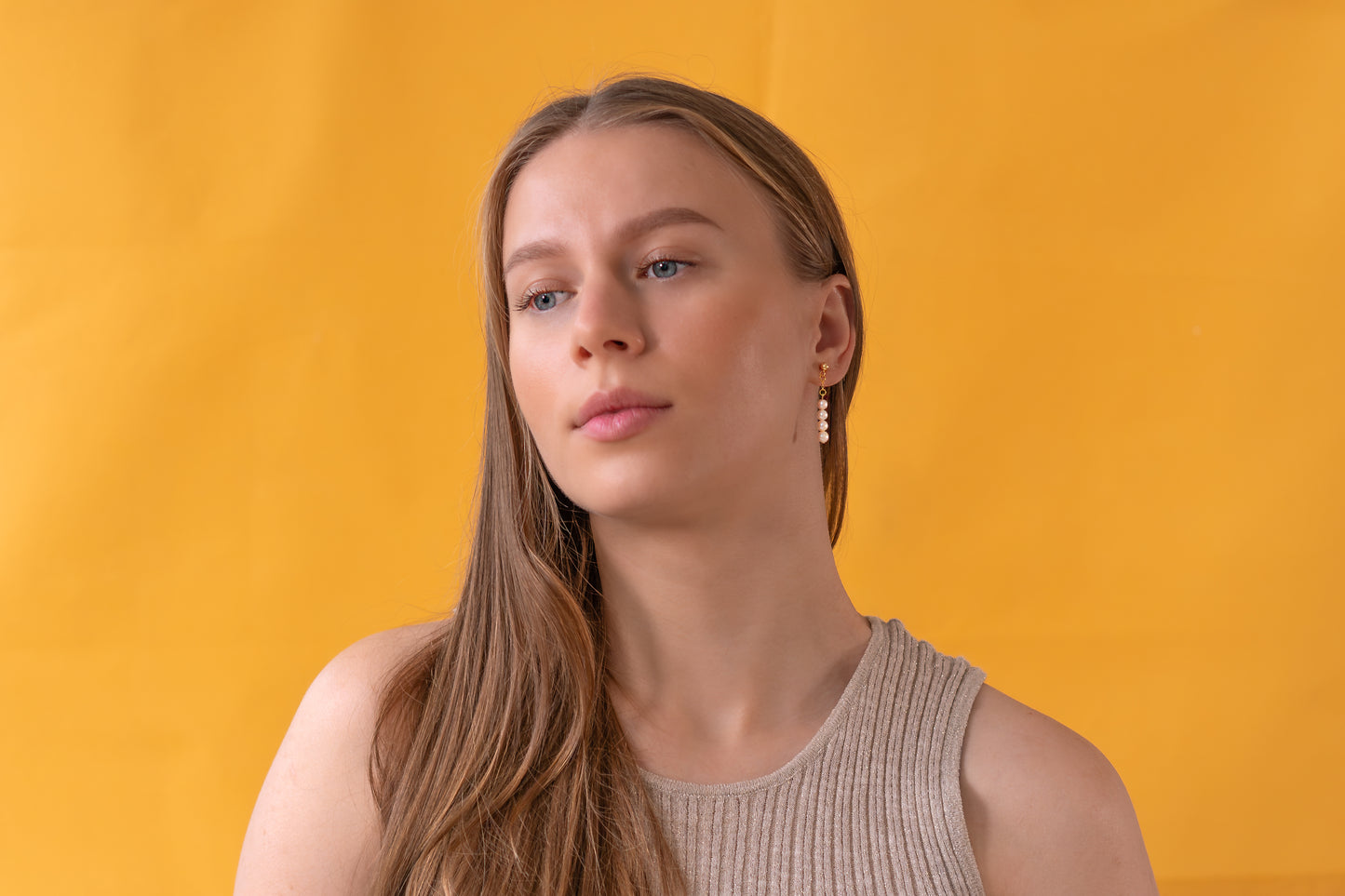 Woman with long hair wearing white pearl earrings against a yellow background
