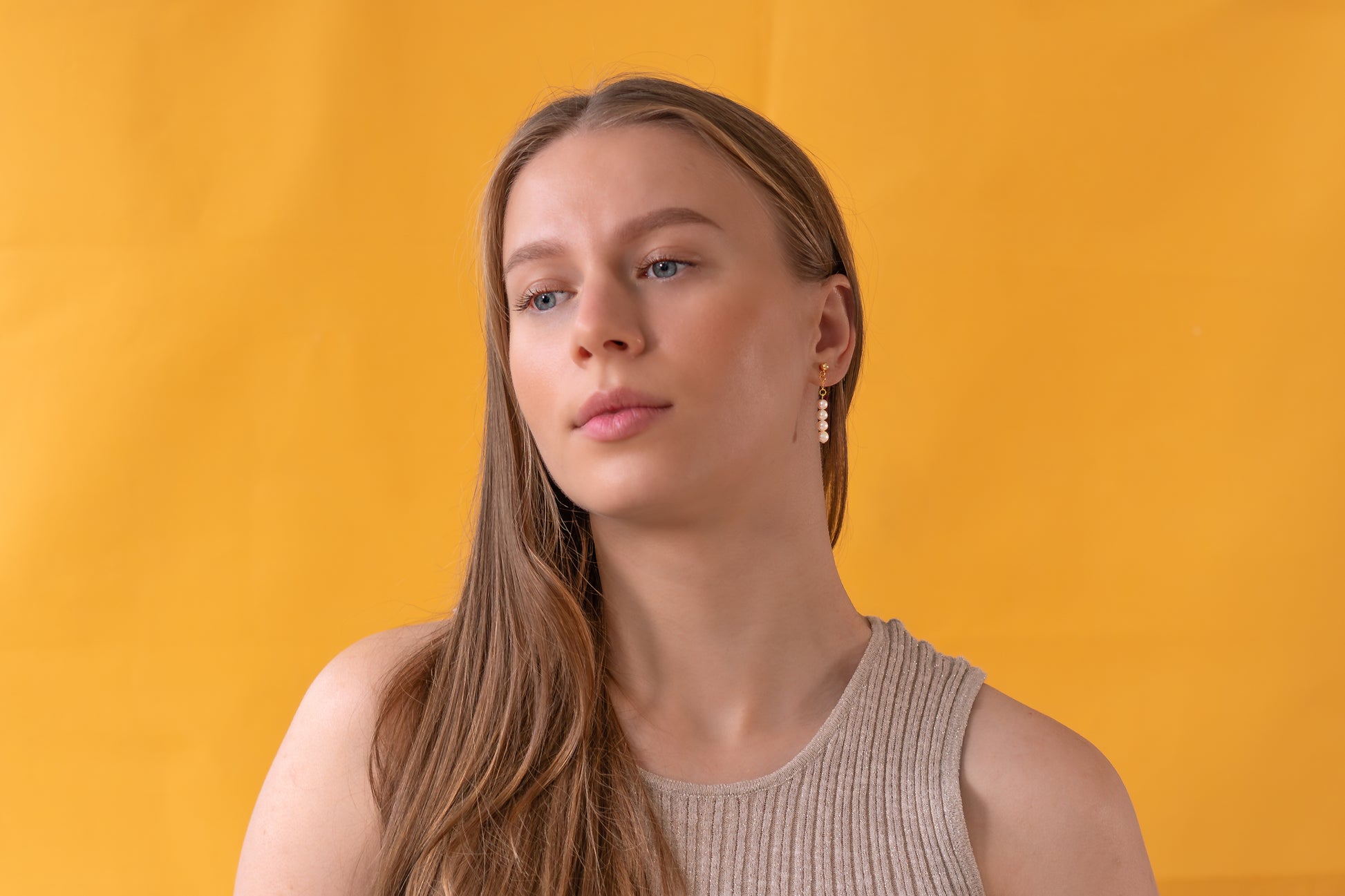 Woman with long hair wearing white pearl earrings against a yellow background