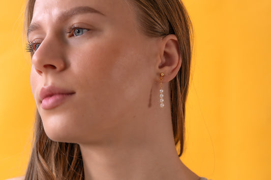 Close-up of a woman wearing white pearl earrings against a yellow background