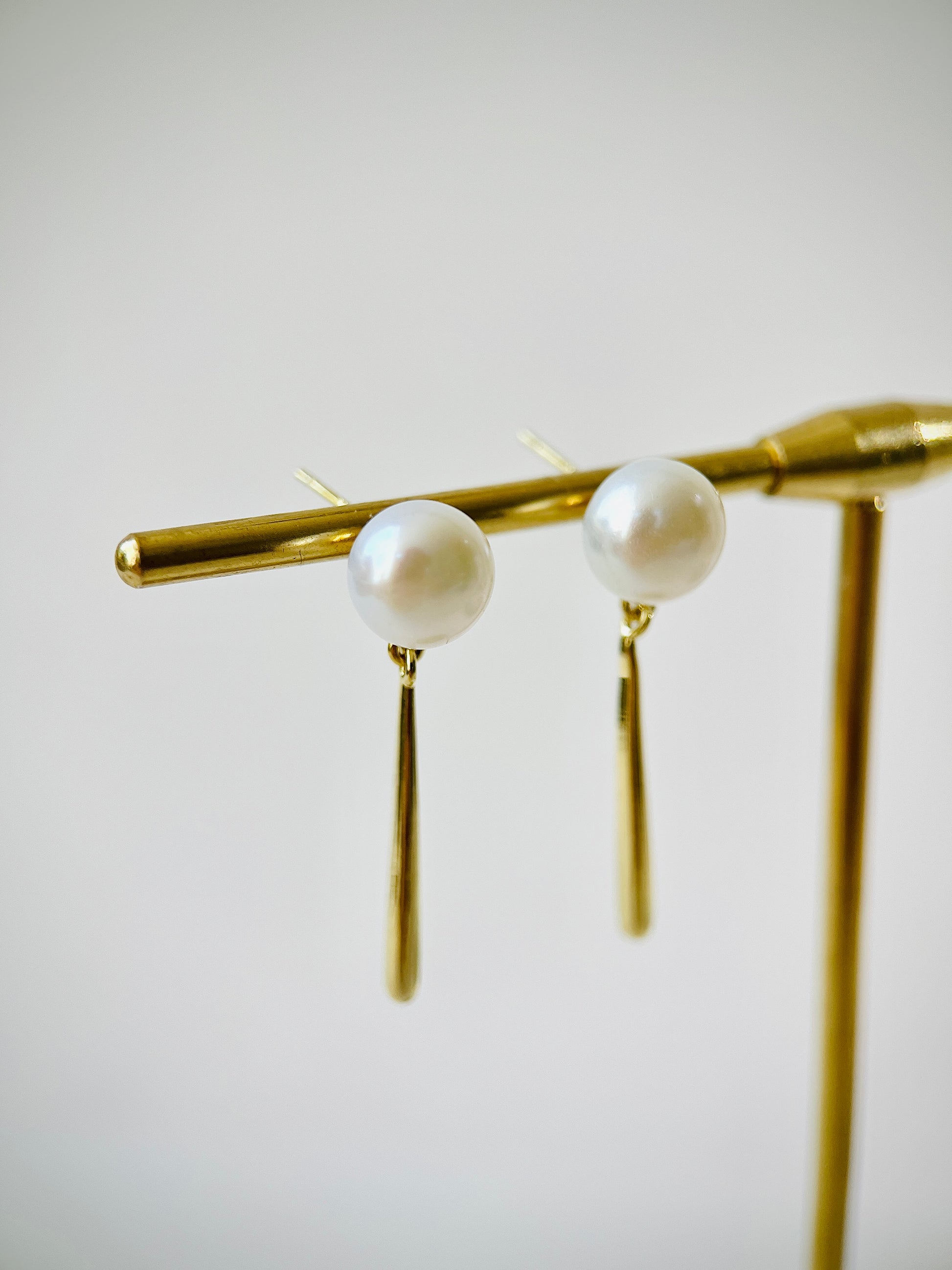Pearl earrings on a gold stand against a light background