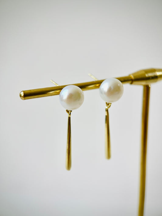 Pearl earrings on a gold stand against a light background