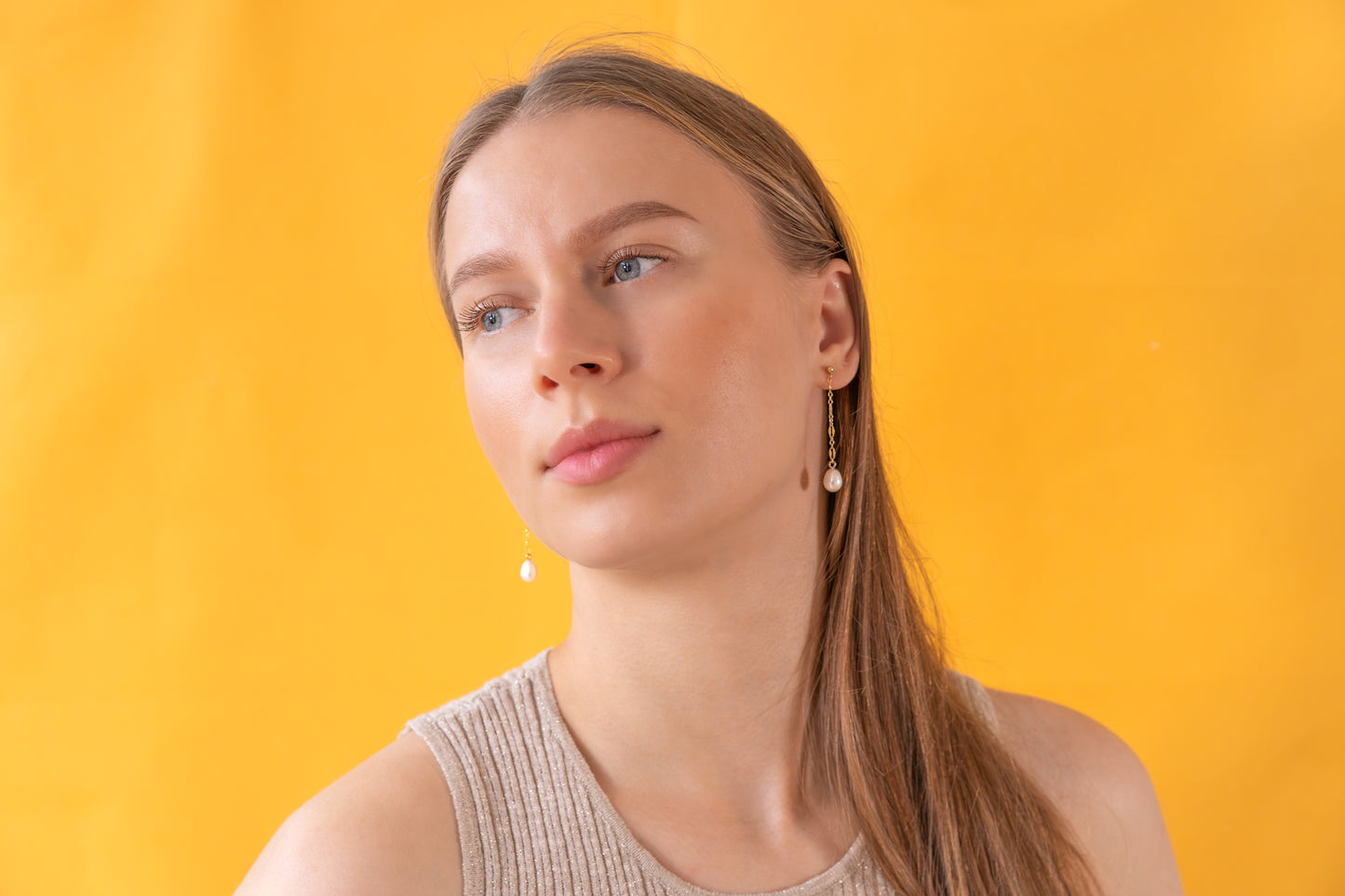 Woman wearing gold earrings with baroque pearl pendants against a yellow background