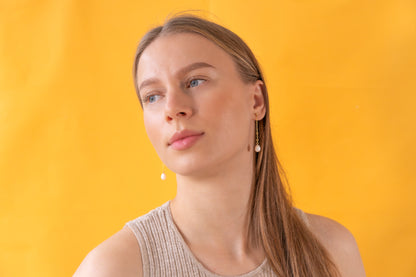 Woman wearing gold earrings with baroque pearl pendants against a yellow background