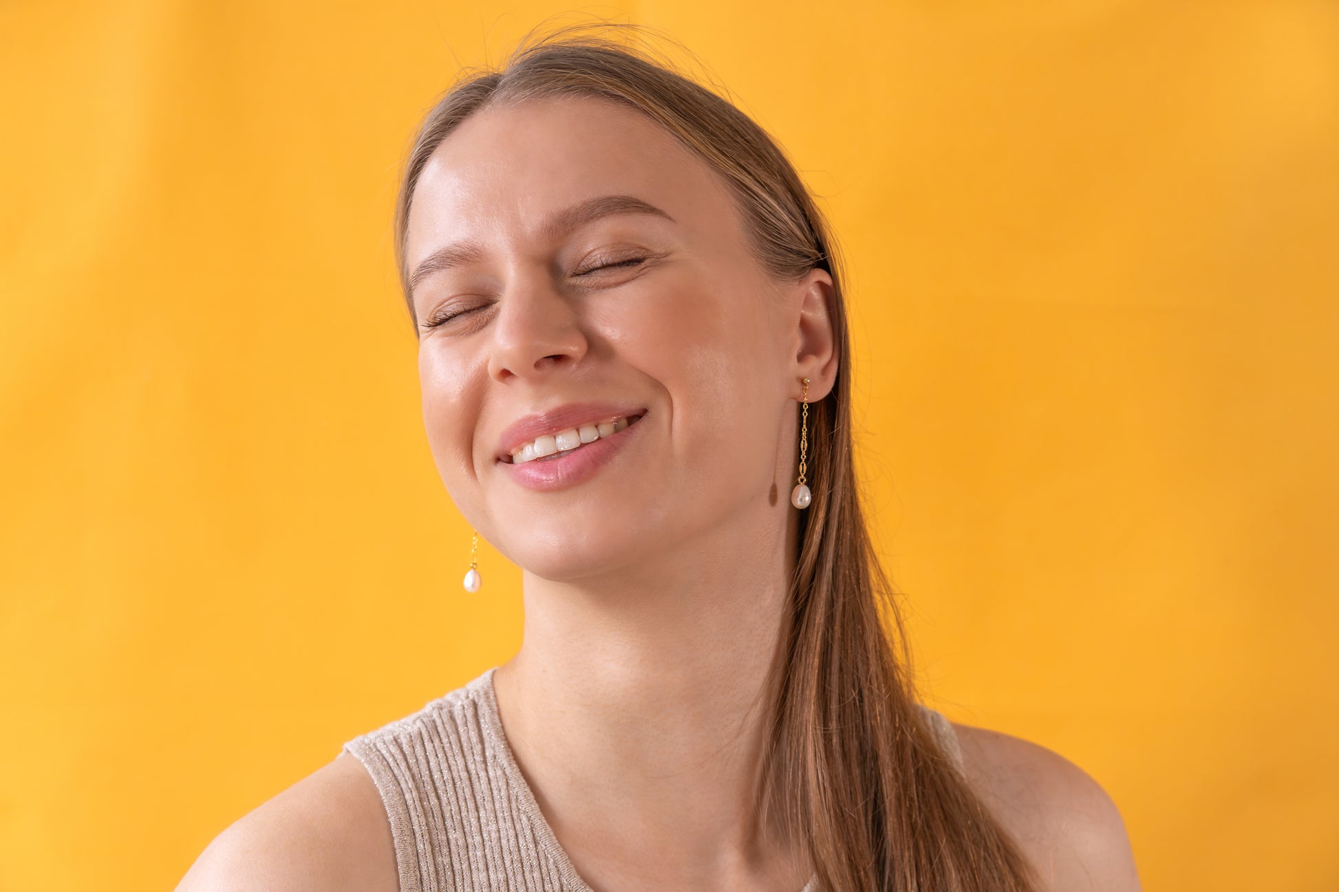 Woman wearing gold earrings with baroque pearl pendants against a yellow background