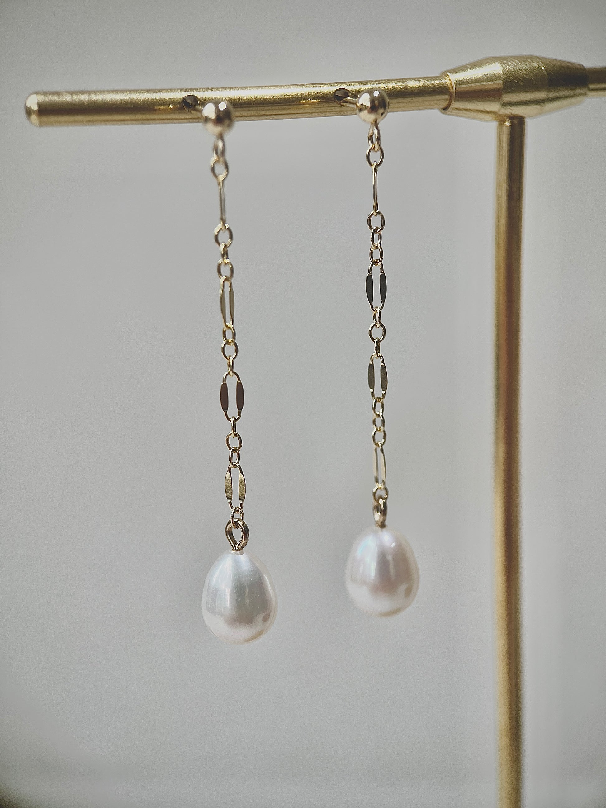 Pearl drop earrings on a gold stand against a neutral background