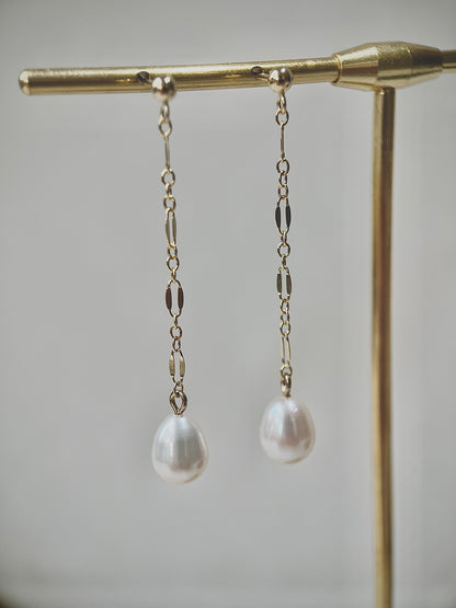 Pearl drop earrings on a gold stand against a neutral background