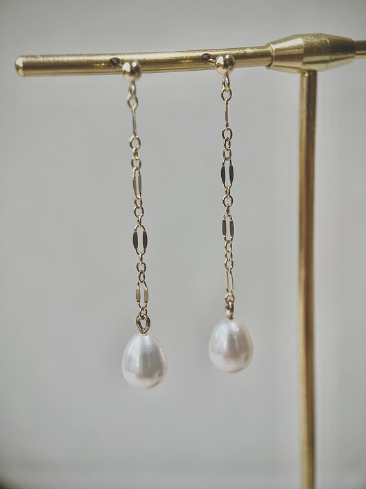 Pearl drop earrings on a gold stand against a neutral background