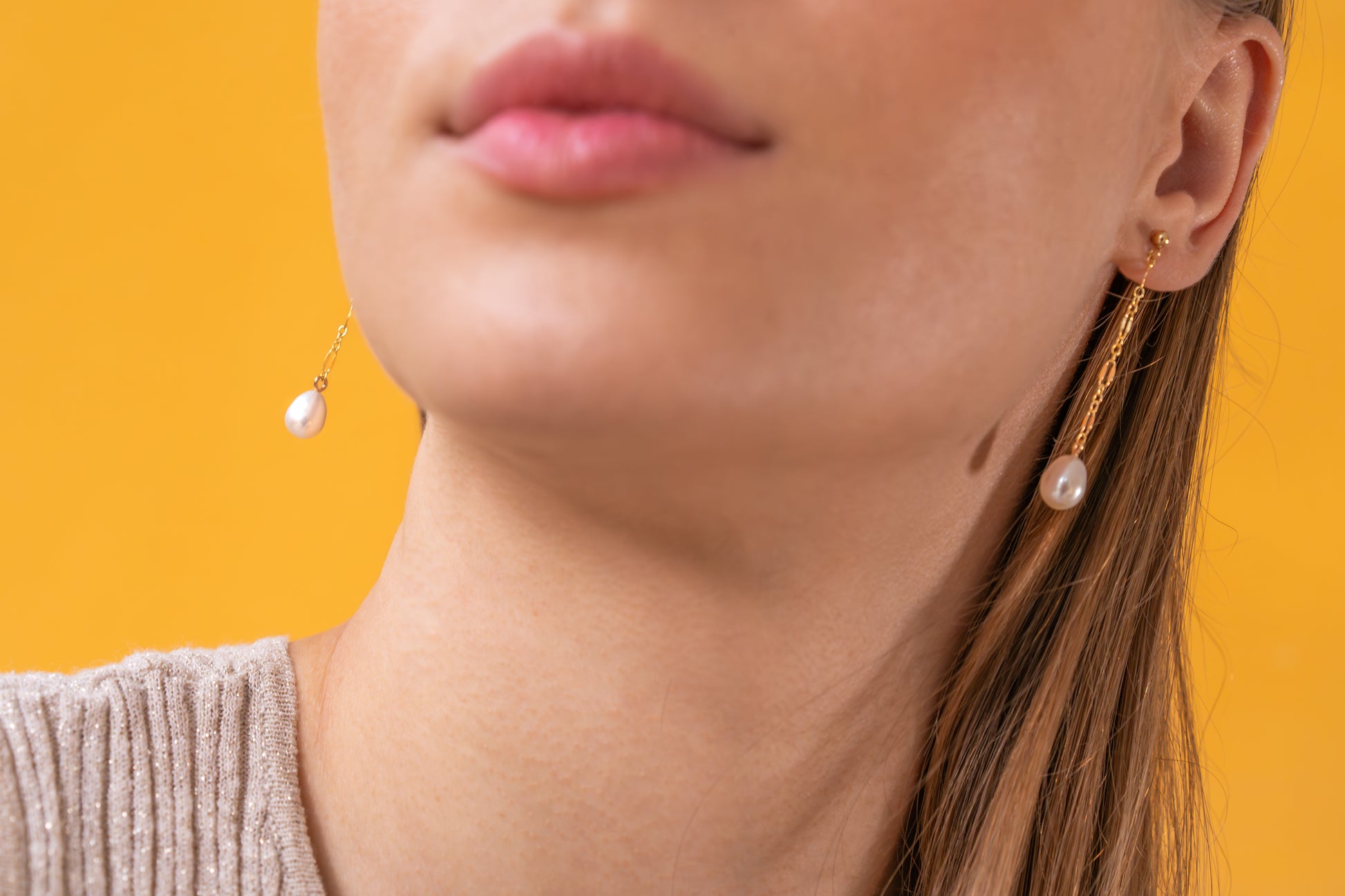 Close-up of a woman wearing gold earrings with pearl drops against a yellow background