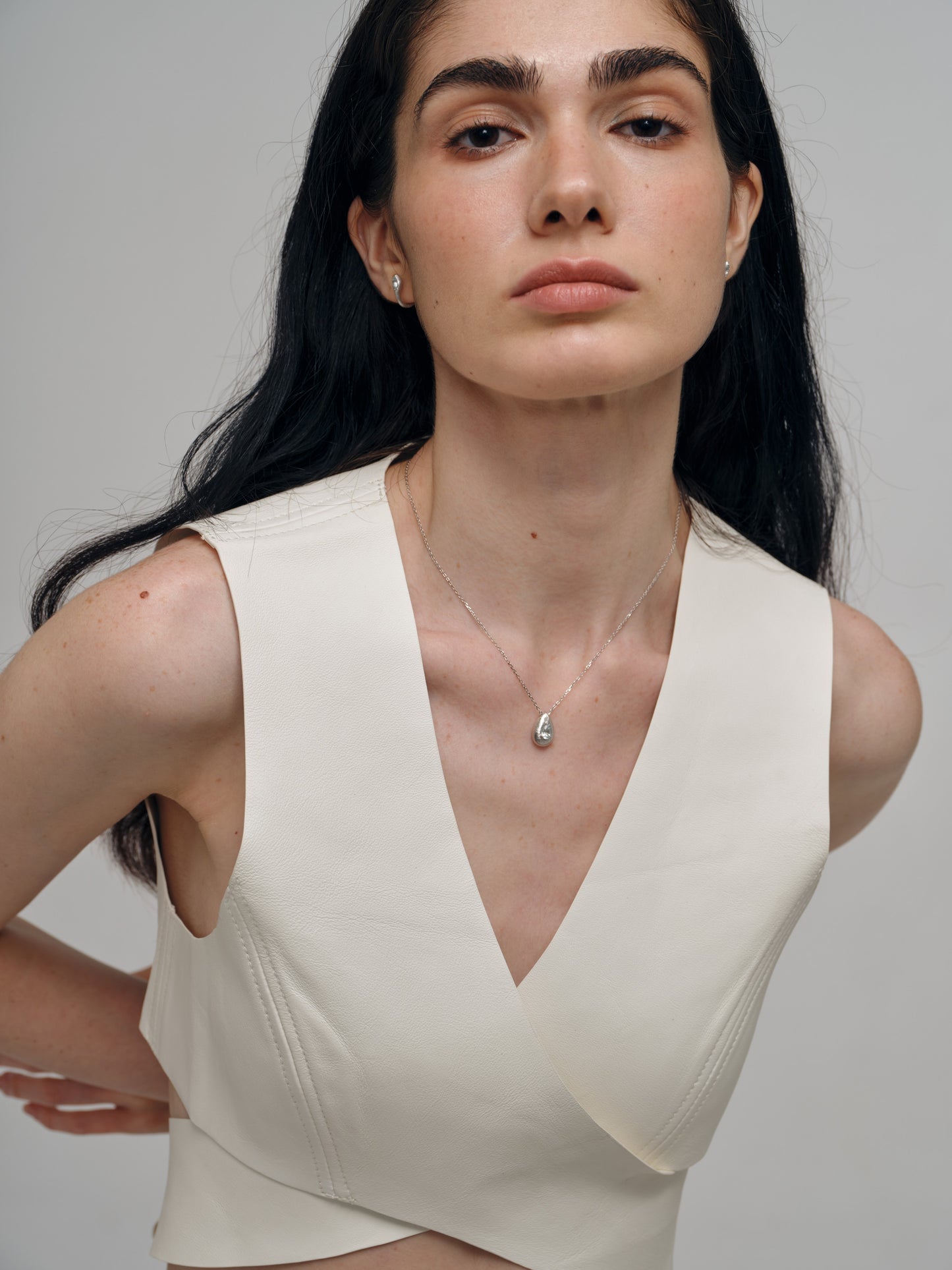 Woman wearing a beige sleeveless top with a aquamarine necklace against a plain background