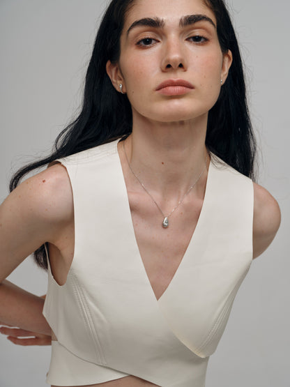 Woman wearing a beige sleeveless top with a aquamarine necklace against a plain background