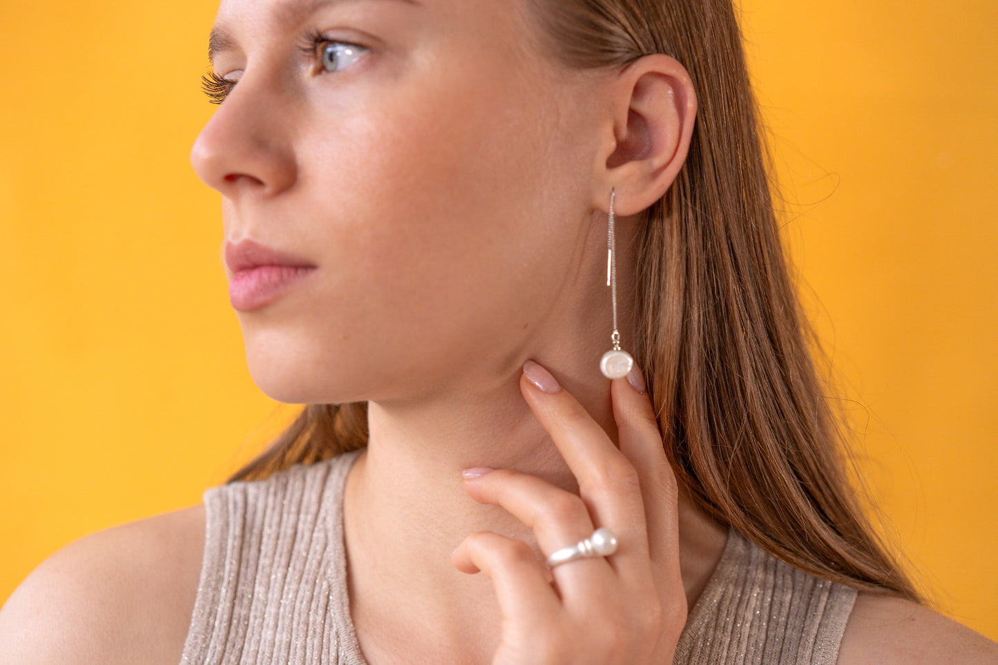 Close-up of a person wearing a silver keshi pearl earring and pearl ring against an orange background