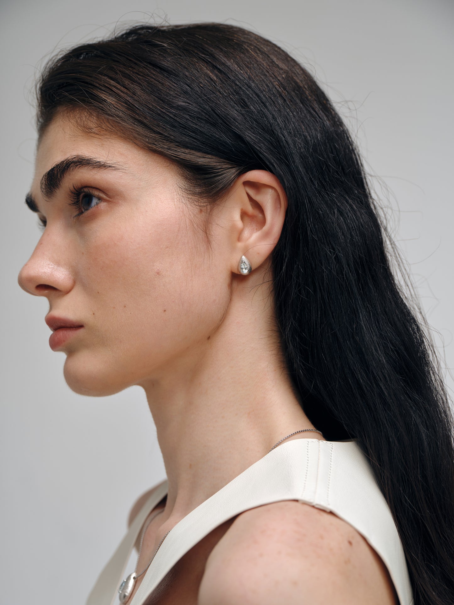 Close-up of a woman's profile wearing aquamarine earrings with a neutral background