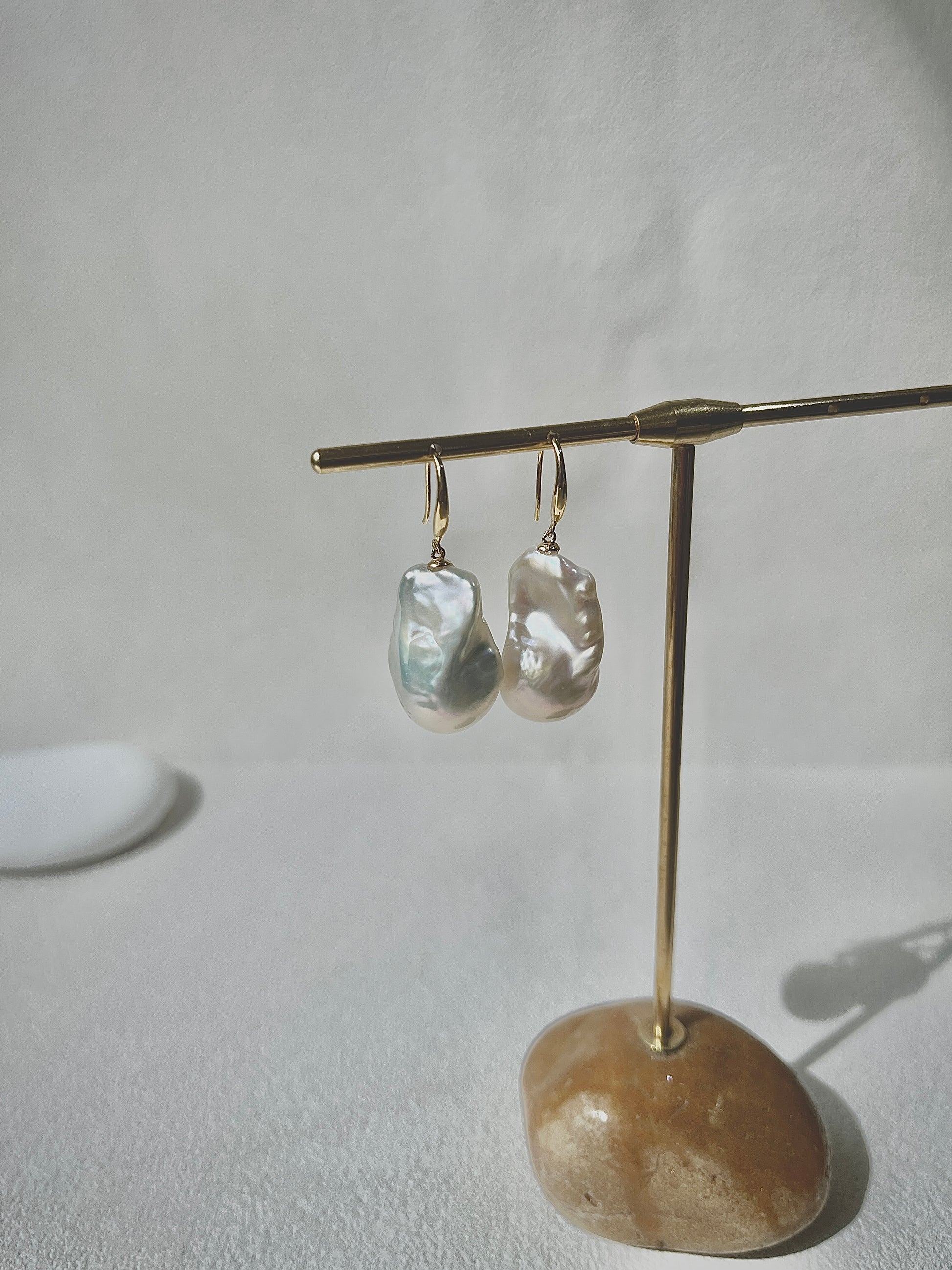 Pair of pearl earrings on a gold stand with a stone base against a white background