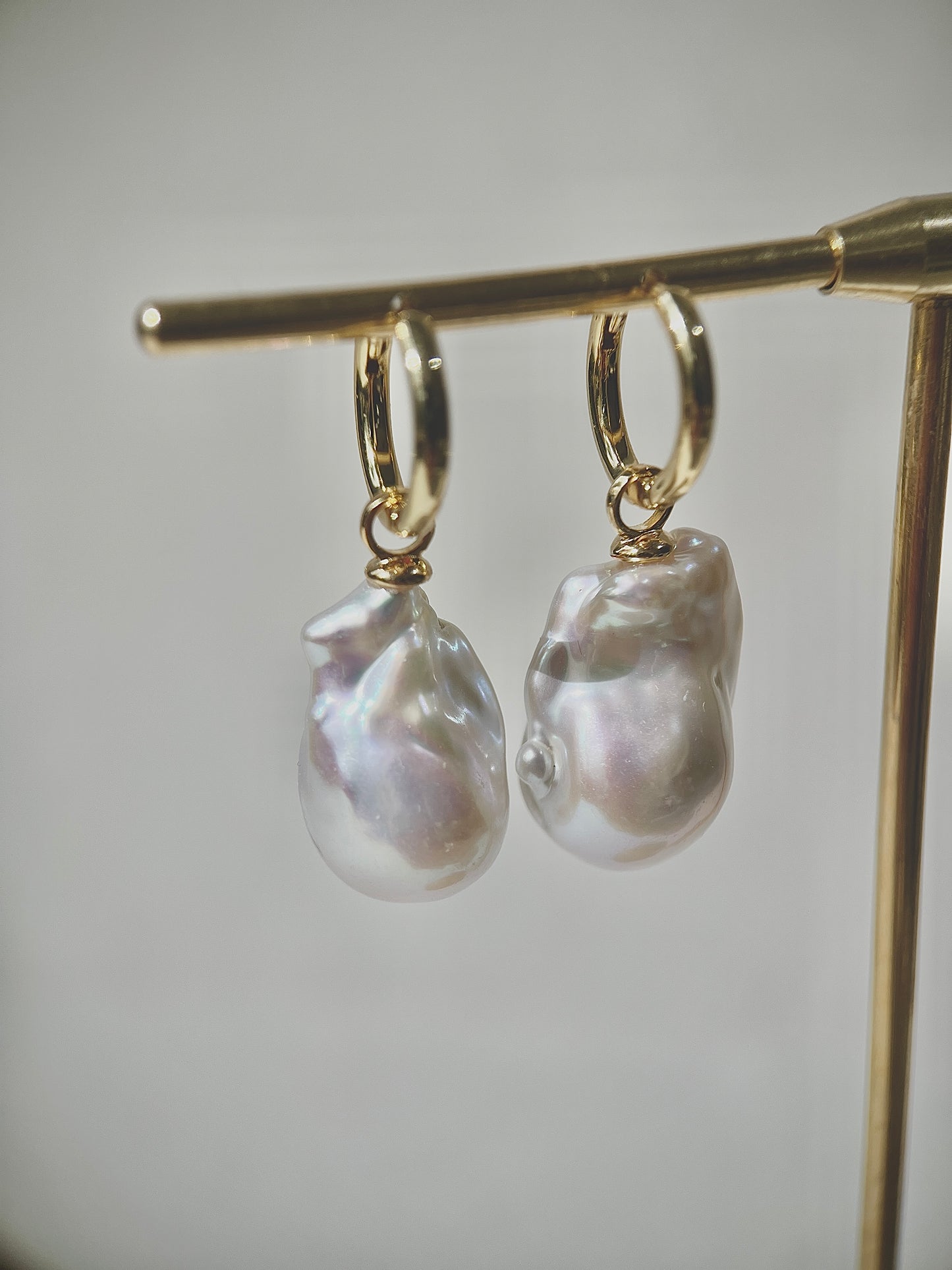 Pearl earrings on a gold stand against a neutral background