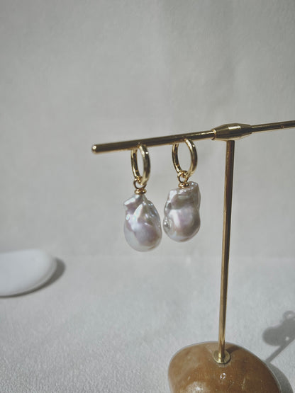 Pearl earrings on a gold stand against a neutral background