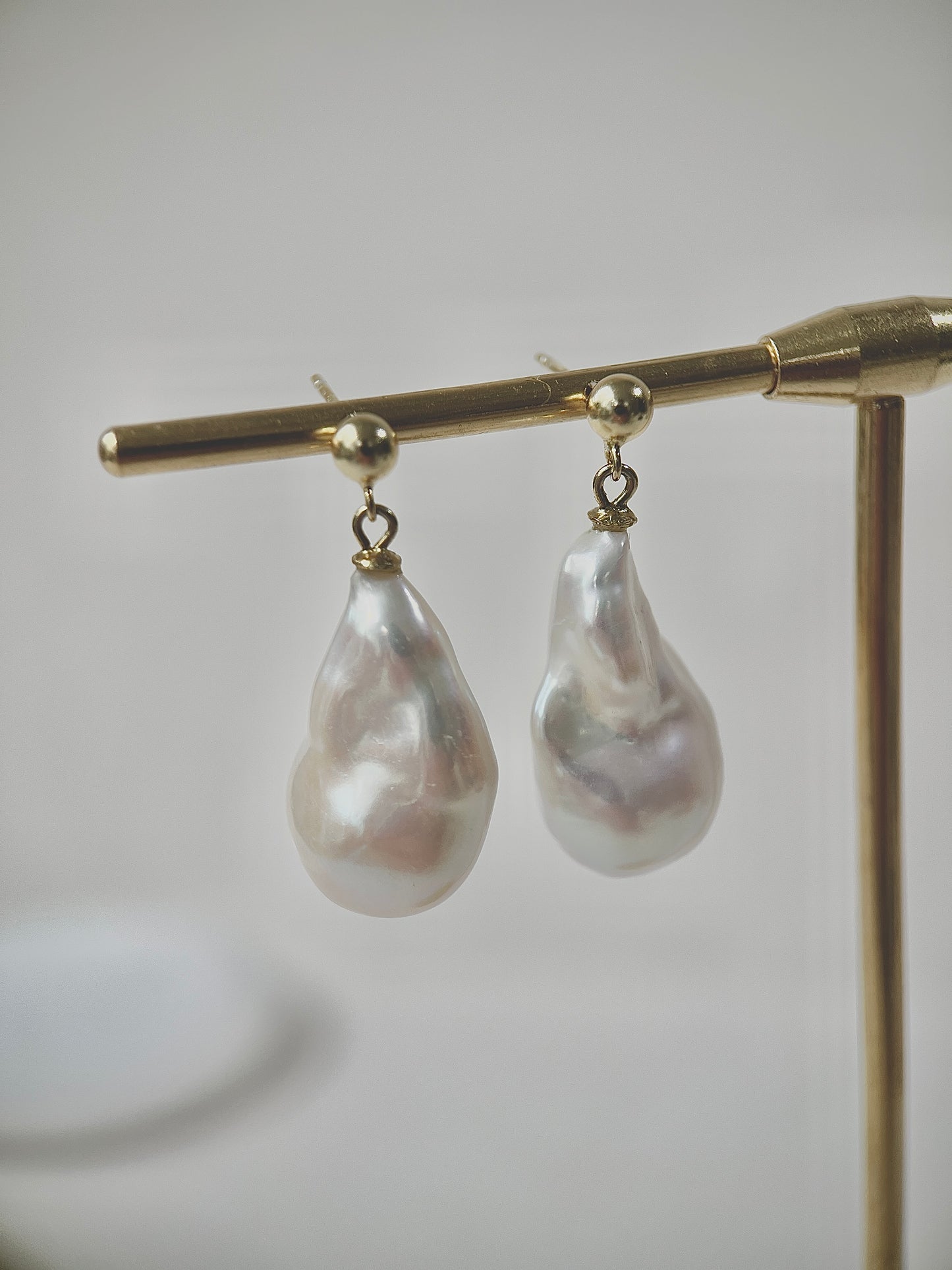 Pearl earrings on a gold stand against a neutral background