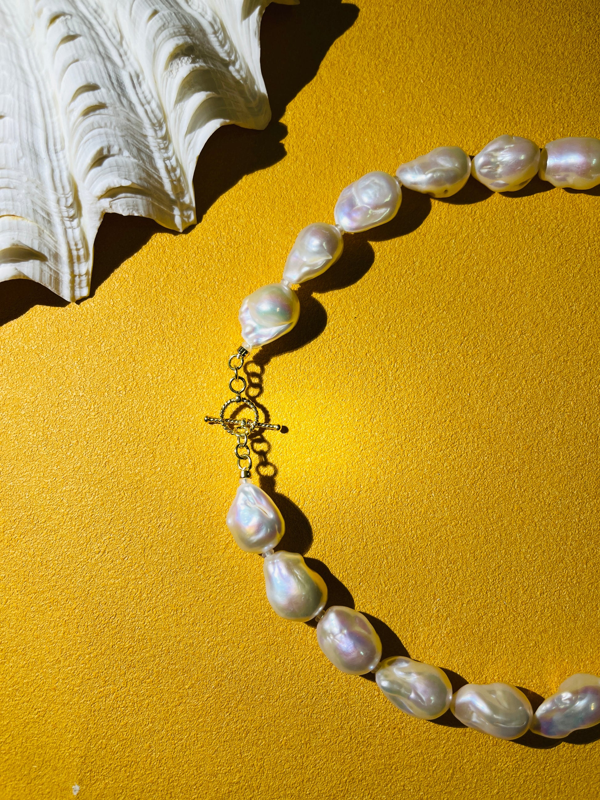 Close-up of a baroque pearl necklace featuring distinct baroque pearls and a gold vermeil clasp on a textured yellow background.